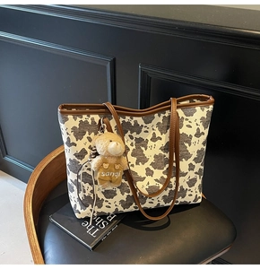 Close-up of cow print tote bag with brown leather handles and a plush bear pendant