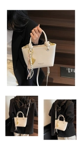 Detailed close-up of cream leather bucket bag with gold branding and woven tassel charm
