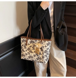 Close-up detail of cow print tote bag featuring a cute teddy bear plush accessory charm