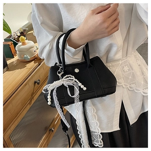 Détail du sac à main noir grainé avec pendentif nœud en dentelle et perles chic