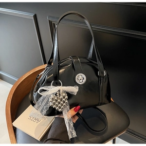 Détail d'un sac à main noir verni avec boucle argentée et pendentif noeud en dentelle