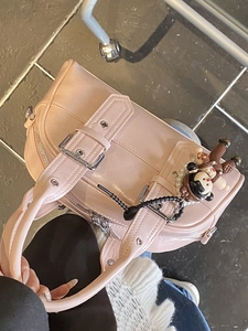 Chic pink faux leather Boston handbag with decorative buckle straps and a cute plush charm
