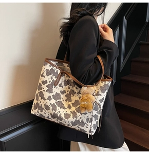 Detail of a large cow print tote bag with brown straps and a cute plush bear charm