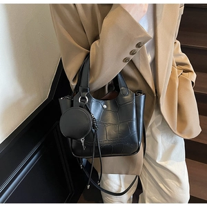 Détail d'un sac seau noir avec texture crocodile et pendentif rond détachable chic