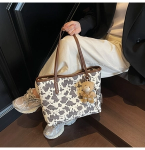Fashionable cow print tote bag with brown leather straps and cute plush bear charm detail