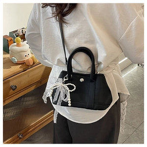 Détail d'un sac seau en cuir noir avec un pendentif nœud en perles et dentelle élégant