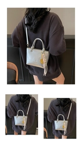 Detail of silver metallic bucket bag featuring tennis racket charm and woven tassel