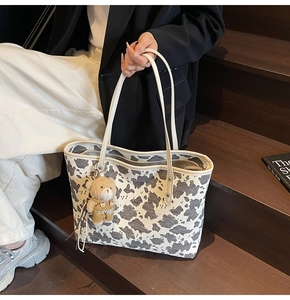 Close-up of cow print tote bag with soft brown bear charm on wooden stairs