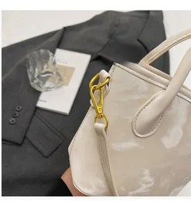 Detail of cream bucket bag showing glossy wave pattern finish and gold buckle