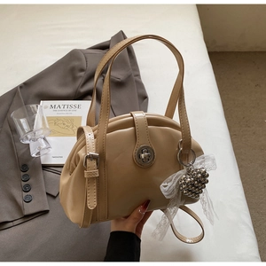 Gros plan du sac coquillage beige en cuir brillant avec pendentif nœud dentelle