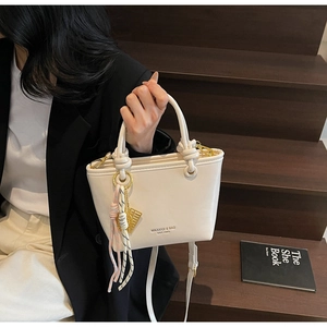 Chic beige leather bucket bag with knot handle and woven charm on outdoor stairs