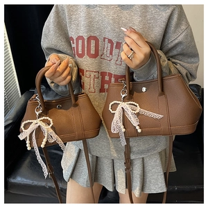 Détail du sac seau en cuir marron texturé avec pendentif nœud en dentelle de perles