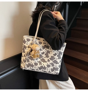 Detail of cow print tote bag with plush bear charm worn by a model in casual setting