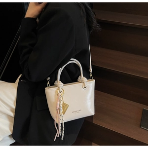 Close-up of cream-white bucket bag with MIKAXIQI logo, gold hardware, and tassel detail