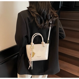 Detail of a beige glossy mini bucket bag featuring brand logo and decorative charms