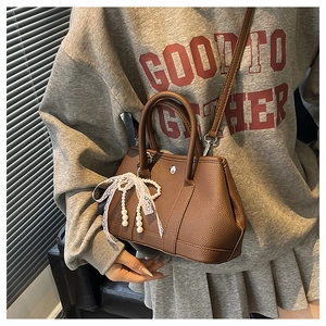 Détail du sac seau en cuir marron à motif litchi avec nœud en dentelle et perle