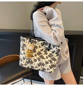 Detail of cow print tote bag featuring a cute brown plush bear charm on the shoulder strap