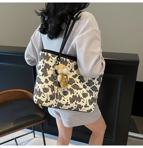 Detail of cow print tote bag featuring a cute brown teddy bear plush charm and slim straps