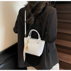 Close-up of a light grey bucket bag with gold branding, silk scarf, and gold pendant details