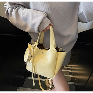 Détail d'un sac seau jaune clair à motif crocodile avec doubles anses et breloque ronde
