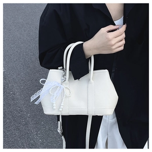 Vue détaillée du sac seau blanc crème texturé avec breloque nœud en dentelle et perles