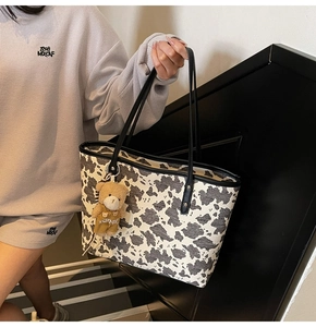 Detail of a large cow print tote bag with black leather straps and cute bear pendant