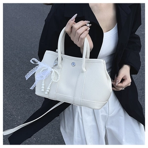 Détail du sac seau en cuir crème avec une élégante breloque en dentelle et perles