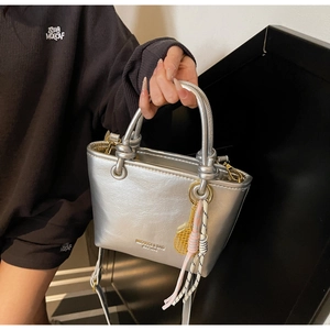 Silver metallic bucket bag with knotted handle, tennis racket charm, and woven strap