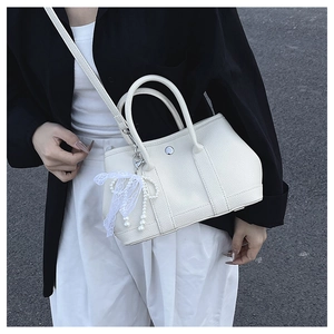 Détail d'un sac seau en cuir crème avec nœud en dentelle et breloque en perles