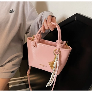Detail of pink patent leather bucket bag with brand logo and knotted top handle