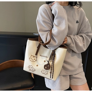 Detail of a large cream tote bag with cat embroidery worn by a model in casual attire