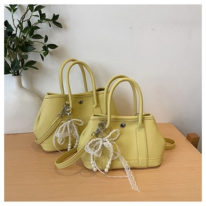 Détail de sacs seaux en cuir jaune avec breloque nœud en dentelle perlée et bandoulière