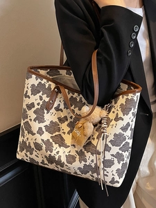 Fashionable cow print tote bag with brown leather trim and cute bear charm on shoulder strap
