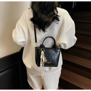 Detailed view of a black glossy leather bucket bag with tassel on a white hoodie model