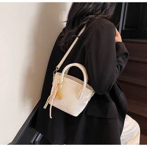 Detail of off-white leather bucket bag featuring a detachable strap and gold tennis racket charm