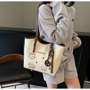 Close-up of cream tote bag featuring cute cartoon embroidery and a pretzel charm accessory