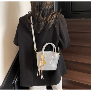 Detail of silver metallic bucket bag featuring golden tennis racket charm and thin strap
