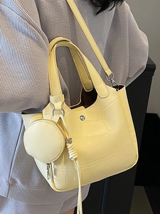 Sac seau en cuir jaune pâle avec motif crocodile et pompon porté par un mannequin