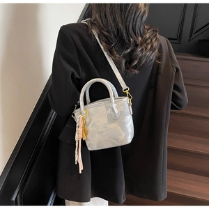 Detail of light gray bucket bag with gold hardware and colorful fringe tassel charm