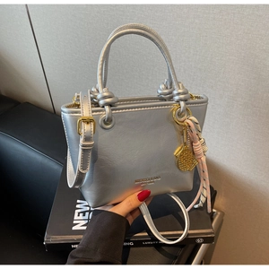 Close-up of metallic silver bucket bag with woven knot and gold tennis racket pendant