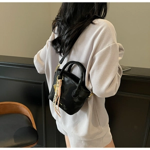 Side view of a black structured bucket bag worn over the shoulder with woven charms