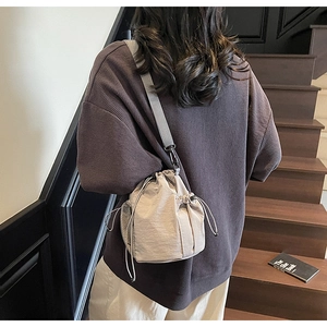 Detail einer beigen Nylon-Beuteltasche mit seitlicher Netztasche und grauem Schultergurt