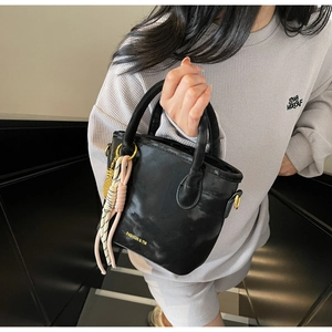 Close-up of black bucket bag featuring golden hardware and decorative braided charms