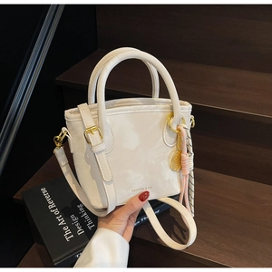 Detail view of white bucket bag with gold tennis racket pendant on wooden stairs