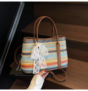 Détail du sac seau en paille arc-en-ciel avec anse en cuir marron et nœud en dentelle