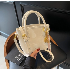 Detail of a beige bucket bag with gold hardware, silk scarf, and logo on a black chair