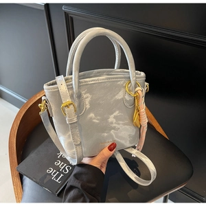 Detail of grey matte textured bucket bag with gold hardware and woven pendant