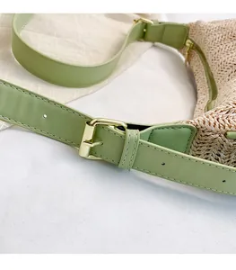 Detailed close-up of woven straw bag featuring green leather strap and gold metal buckle