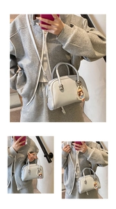 Close-up of a light gray square handbag with a cute pearl doll charm and top handle