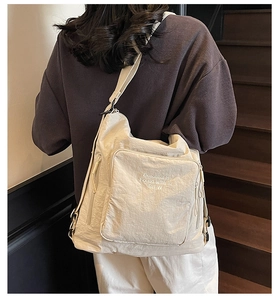 Detail view of cream nylon tote bag featuring white embroidery on a textured surface